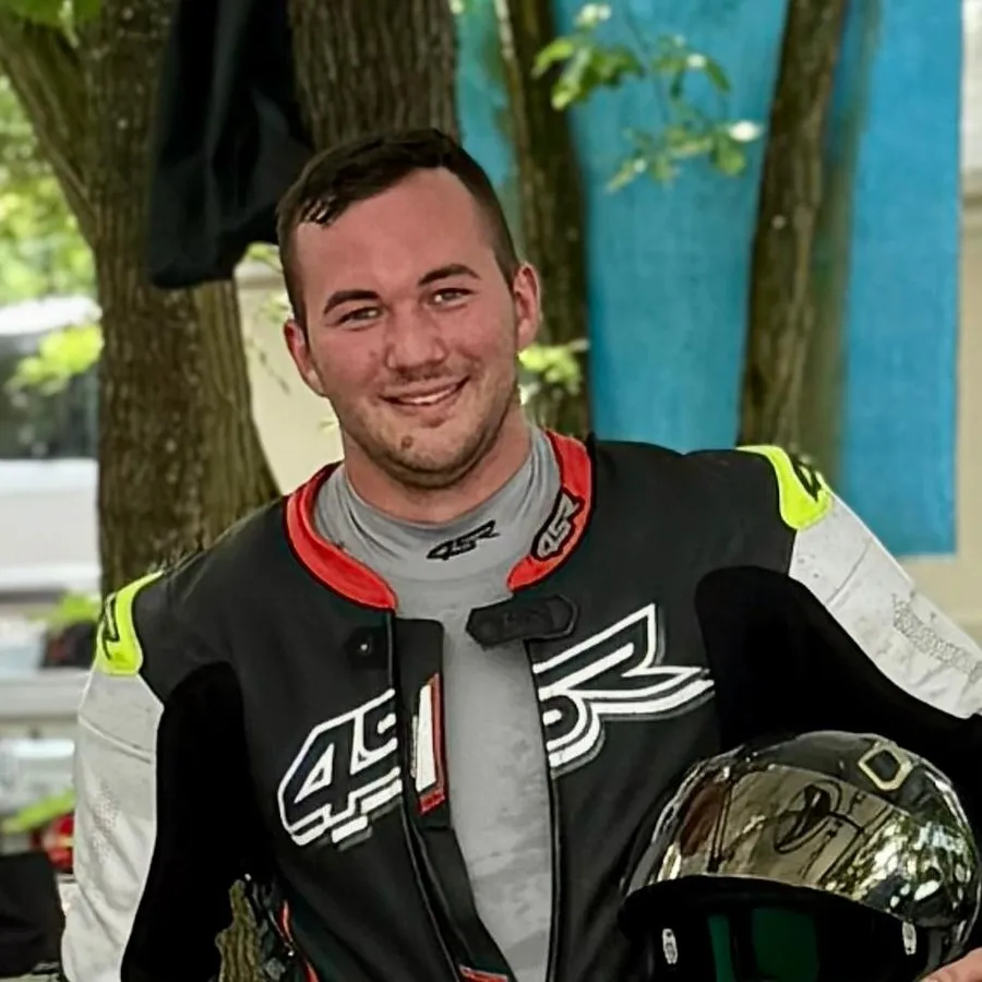 Aaron in schwarz-weissem Lederkombi mit Helm im Arm unter einem Fahrerlagerzelt